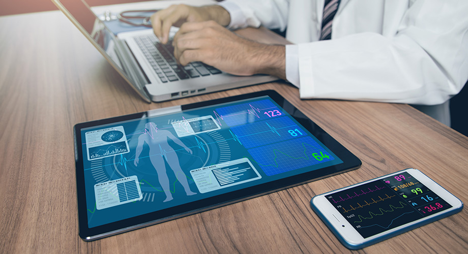 Physician typing on laptop next to tablet and smartphone